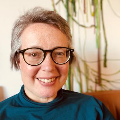 Woman with short hair, glasses with black frames, and teal roll-neck top